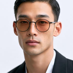 May include: Round-frame glasses featuring thin, dark matte frames and light amber-tinted lenses. The eyewear has a minimalist bridge design and slim temples, providing a clear view of the circular lens shape and the dark metal construction.