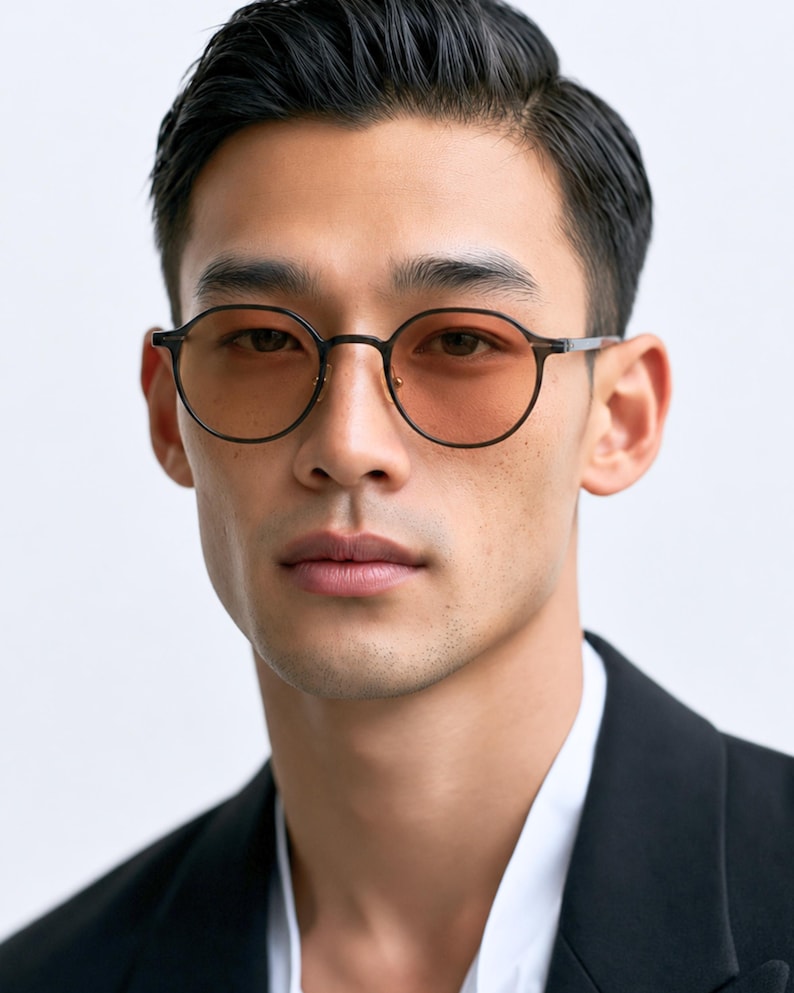 May include: Round-frame glasses featuring thin, dark matte frames and light amber-tinted lenses. The eyewear has a minimalist bridge design and slim temples, providing a clear view of the circular lens shape and the dark metal construction.