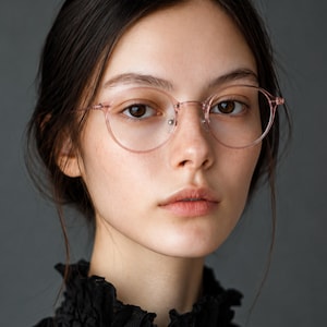 May include: Round eyeglasses featuring a translucent, pale pink plastic frame with thin, matching temples. The design includes a classic bridge and integrated nose pads, providing a clear, lightweight look that frames the face with a soft color.