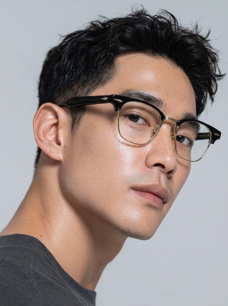 May include: Spectacles featuring a black browline frame with gold-tone metal rims and bridge. The temples are black with a small gold-tone arrow-shaped accent at the hinge. The lenses are clear and the overall design is a classic semi-rimless style.