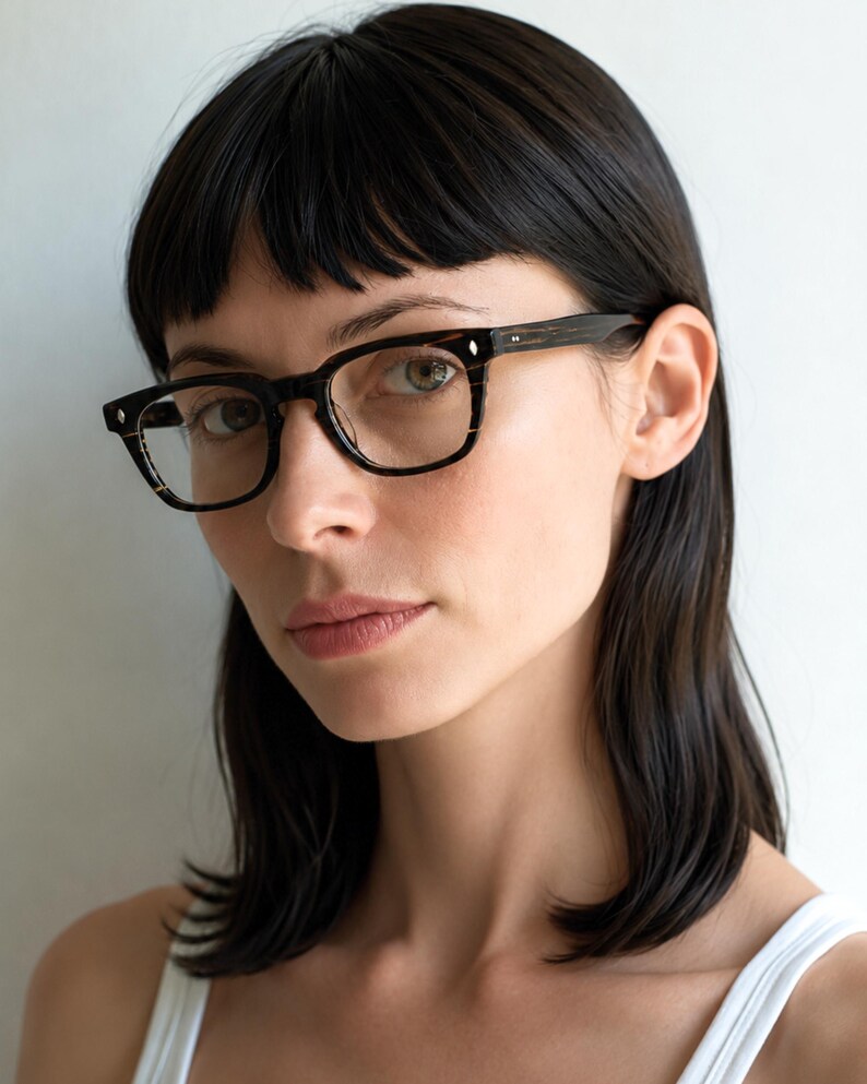 May include: Full-rim eyeglasses featuring a dark brown and black tortoiseshell pattern frame. The rectangular lenses are clear, and the frame includes small silver-toned metal rivets on the front corners and temples for a classic, structured look.