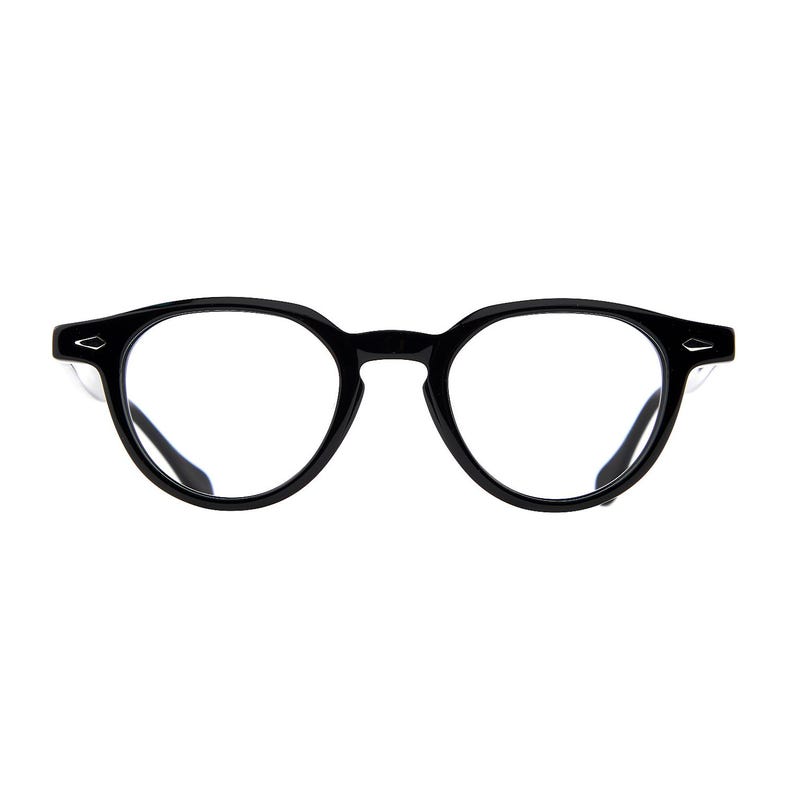 May include: Black eyeglasses with a round frame design. The glasses have a thick, glossy black frame and clear lenses. The temples have a small, silver accent. The overall style is classic and modern.