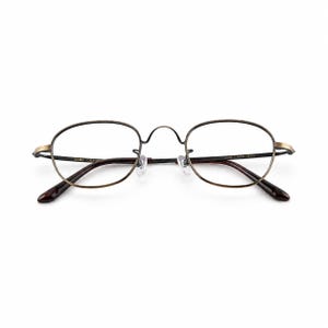 May include: Oval-shaped eyeglasses with a thin, bronze-colored metal frame. The lenses are clear, and the temples are a dark brown color. The glasses have a classic, vintage design.