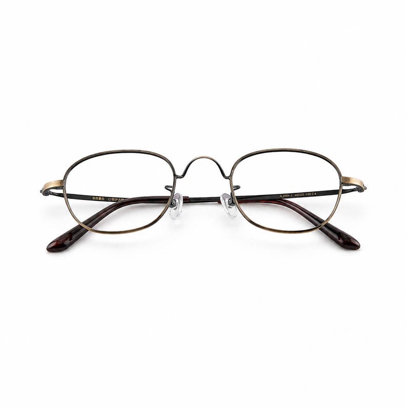 May include: Oval-shaped eyeglasses with a thin, bronze-colored metal frame. The lenses are clear, and the temples are a dark brown color. The glasses have a classic, vintage design.