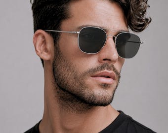 May include: Silver-toned metal sunglasses featuring a double bridge design and square-shaped dark grey lenses. The frames have thin, straight temples and adjustable nose pads, providing a clean and structured look for these classic eyewear pieces.