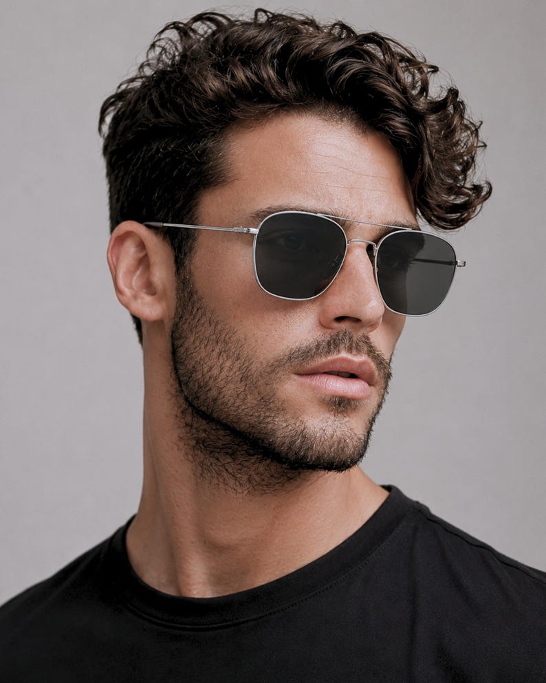 May include: Silver-toned metal sunglasses featuring a double bridge design and square-shaped dark grey lenses. The frames have thin, straight temples and adjustable nose pads, providing a clean and structured look for these classic eyewear pieces.