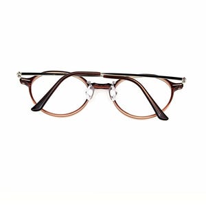 May include: Round eyeglasses featuring a dark brown frame with a subtle gradient effect, thin silver-toned metal temples, and clear lenses. The design includes adjustable nose pads and dark brown temple tips, providing a clear view of the frame structure.
