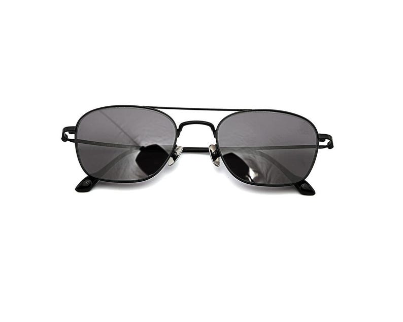 May include: Black metal frame sunglasses featuring a double bridge design and dark grey tinted lenses. The eyewear has thin, minimalist temples and adjustable nose pads, providing a sleek and functional look for eye protection against sunlight.