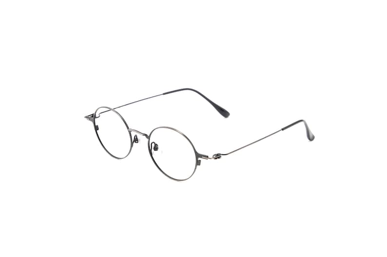 May include: Round eyeglasses featuring a thin, dark metallic frame with a bridge, adjustable nose pads, and slender temples that curve at the ends. The lenses are clear and circular, held in place by a lightweight wire structure that connects to the arms.