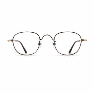 May include: Round eyeglasses with a dark brown metal frame and clear lenses. The temples and nose bridge are a lighter gold color. The lenses have a slight tint of brown. The glasses are designed for vision correction.