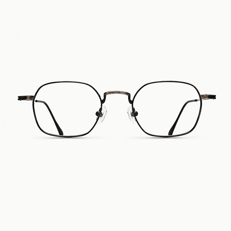 May include: Eyeglasses with a thin, dark metallic frame featuring a rounded square shape. The glasses have clear lenses, a bridge connecting the two rims, and adjustable nose pads. The temples extend outward from the sides of the frame.