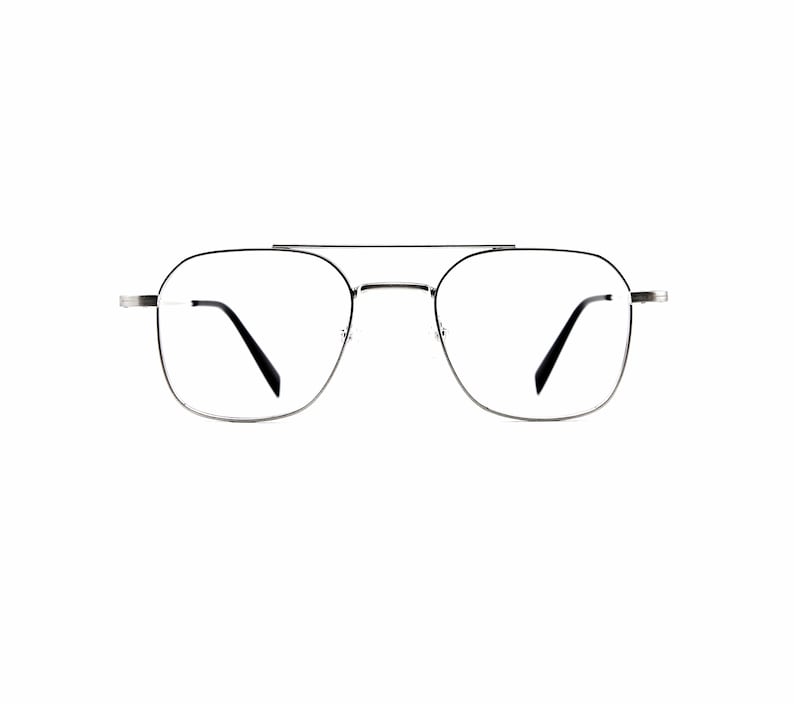 May include: Silver-toned metal eyeglasses featuring a double bridge design with a thin, rectangular frame shape. The glasses have clear lenses and black temple tips, providing a clean and structured look for the wearer's face.