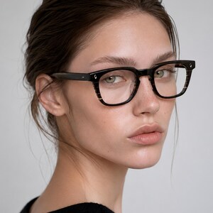 May include: Rectangular eyeglasses featuring a dark brown and black striped acetate frame with a glossy finish. The glasses have clear lenses, a thick bridge, and small silver-toned metal accents on the outer corners of the front frame.