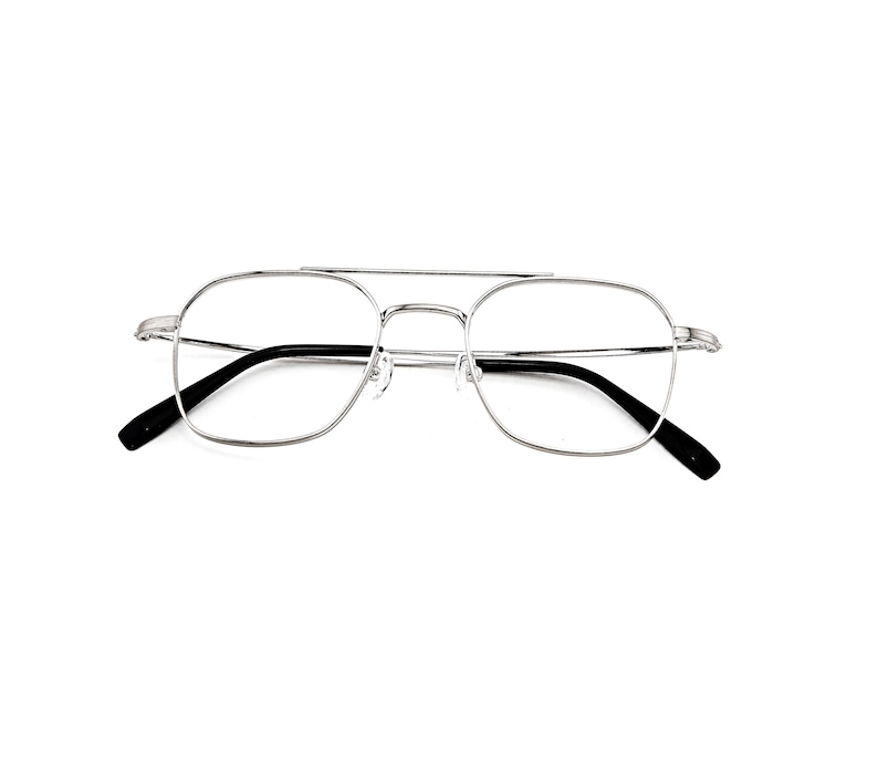 May include: Silver-toned metal eyeglasses featuring a double bridge design with a thin, rectangular frame shape. The glasses have clear lenses and black temple tips, providing a clean and structured look for the wearer's face and eyes.