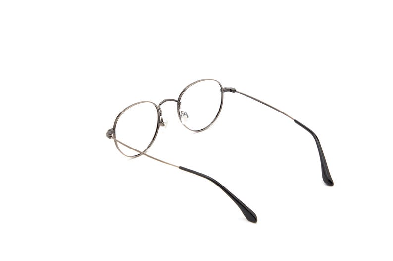 Puede incluir: Un par de gafas con monturas redondas y finas de metal color gris plomo y lentes transparentes. Las varillas son delgadas y oscuras, con puntas de pl&aacute;stico negro en los extremos. El puente es curvo, uniendo los dos aros circulares.