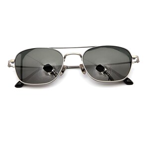 May include: Silver-toned metal frame sunglasses featuring a double bridge design and dark gray tinted lenses. The rectangular-shaped lenses are encased in a thin metallic rim with matching silver temples and black plastic temple tips at the ends.