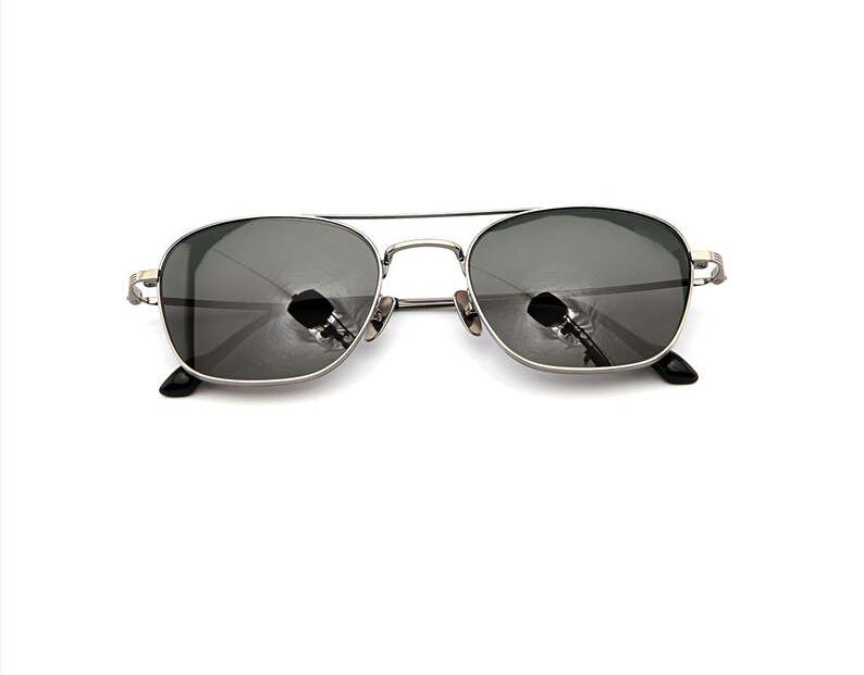 May include: Silver-toned metal frame sunglasses featuring a double bridge design and dark gray tinted lenses. The rectangular-shaped lenses are encased in a thin metallic rim with matching silver temples and black plastic temple tips at the ends.