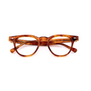 Puede incluir: Gafas marrones con montura de carey y dise&ntilde;o cl&aacute;sico redondeado. Las gafas tienen un puente de cerradura y est&aacute;n sobre un fondo blanco. El texto "COMMONWEALTH" y "48022-148 COL.A" es visible en la montura.
