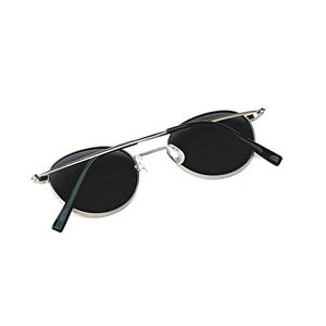 May include: Oval sunglasses with dark lenses and a silver metal frame. The temples are thin and silver, with dark green tips. The sunglasses are set against a white background.