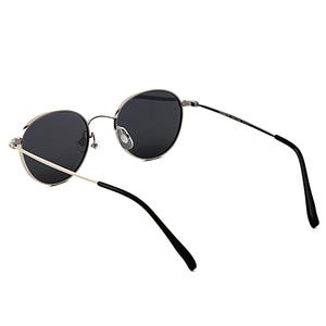 May include: Round sunglasses with dark lenses and a silver frame. The temples are thin and black, with a silver hinge. The sunglasses are set against a white background.