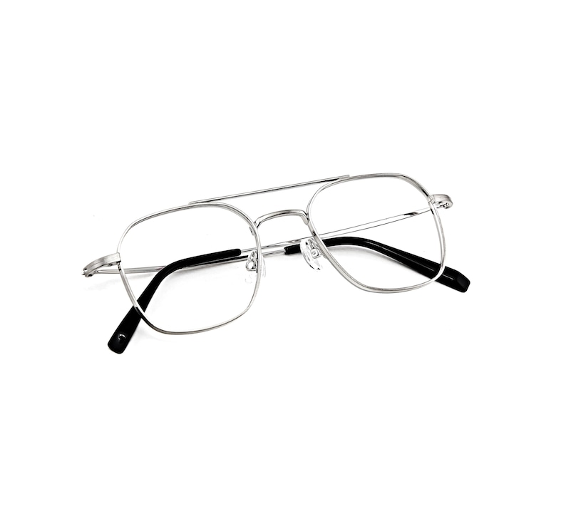 May include: Silver-toned metal eyeglasses featuring a double bridge design and a square frame shape. The glasses have clear lenses and black temple tips, providing a clean and structured look with adjustable nose pads for a secure fit.