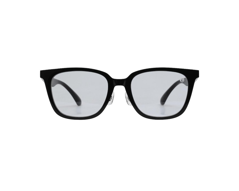 K&ouml;nnte beinhalten: Brille mit schwarzem Rahmen und quadratischer Form. Die Gl&auml;ser sind klar und die B&uuml;gel sind nach innen gebogen. Die Brille ist vor einem wei&szlig;en Hintergrund platziert, was ihr schlankes Design hervorhebt. Ein klassisches Brillenaccessoire.