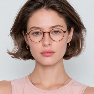 May include: Round eyeglasses with a thin, translucent brown frame and metallic temples. The glasses feature a classic circular lens shape with a bridge and nose pads, providing a clear view of the frame structure and the overall design of the eyewear.