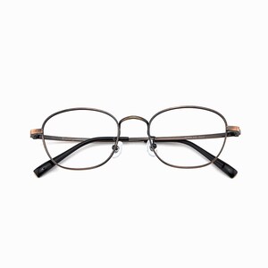 May include: Oval spectacles with a bronze-coloured metal frame and black temples. The lenses are clear, and the nose bridge is thin. The glasses have a classic, vintage aesthetic.