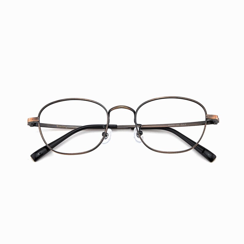 May include: Oval spectacles with a bronze-coloured metal frame and black temples. The lenses are clear, and the nose bridge is thin. The glasses have a classic, vintage aesthetic.