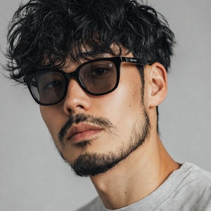 May include: Black-framed eyeglasses with tinted lenses. The glasses have a round shape and are worn by a person with dark hair and a beard. The person is wearing a gray crew neck shirt.