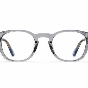 May include: Gray, round-framed eyeglasses with clear lenses. The frames have a translucent appearance, with a subtle gradient on the temples, transitioning from gray to blue. The glasses are set against a plain white background.