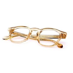 Puede incluir: Un par de gafas transparentes de color marr&oacute;n claro con una montura cuadrada redondeada cl&aacute;sica. Las gafas tienen una calidad sutil y transl&uacute;cida, y las patillas son de un tono marr&oacute;n m&aacute;s oscuro. Las lentes son claras.