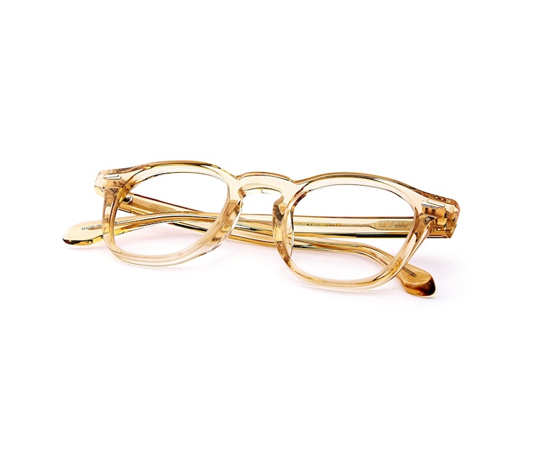 Puede incluir: Un par de gafas transparentes de color marr&oacute;n claro con una montura cuadrada redondeada cl&aacute;sica. Las gafas tienen una calidad sutil y transl&uacute;cida, y las patillas son de un tono marr&oacute;n m&aacute;s oscuro. Las lentes son claras.