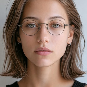 May include: Round spectacles with a thin, dark metallic frame and clear lenses. The glasses feature a simple bridge design and slender temples that extend to the sides, providing a clean and functional look for everyday vision correction needs.
