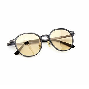 May include: Round eyeglasses featuring a dark translucent grey frame and light amber tinted lenses. The glasses have a thin bridge, metallic nose pads, and slender temples with visible hinges, presenting a clear view of the front and side profile.