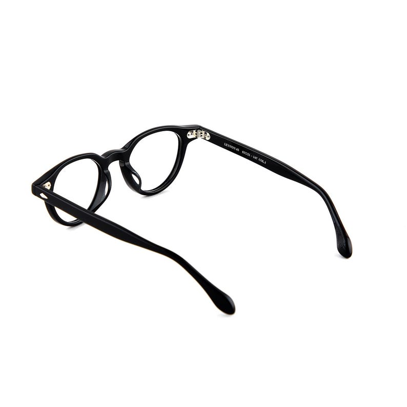 May include: Black eyeglasses with round frames. The glasses have a matte finish and a sleek, modern design. The temples are thin and curve gently towards the ear. The text on the temple reads: LENOX 60 50033 - 147 COL. E.