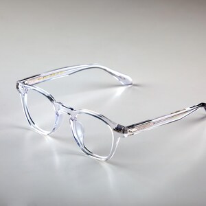 K&ouml;nnte beinhalten: Klare Brille mit quadratischem Rahmen und transparentem Design. Die Brille hat eine klassische Form mit einer dezenten, modernen &Auml;sthetik. Rahmen und B&uuml;gel bestehen aus transparentem Material.