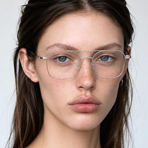 May include: Silver-toned metal eyeglasses featuring a thin, rectangular frame with rounded corners and a prominent double bridge design. The glasses have slender temples and adjustable nose pads, providing a clean, metallic aesthetic for the face.