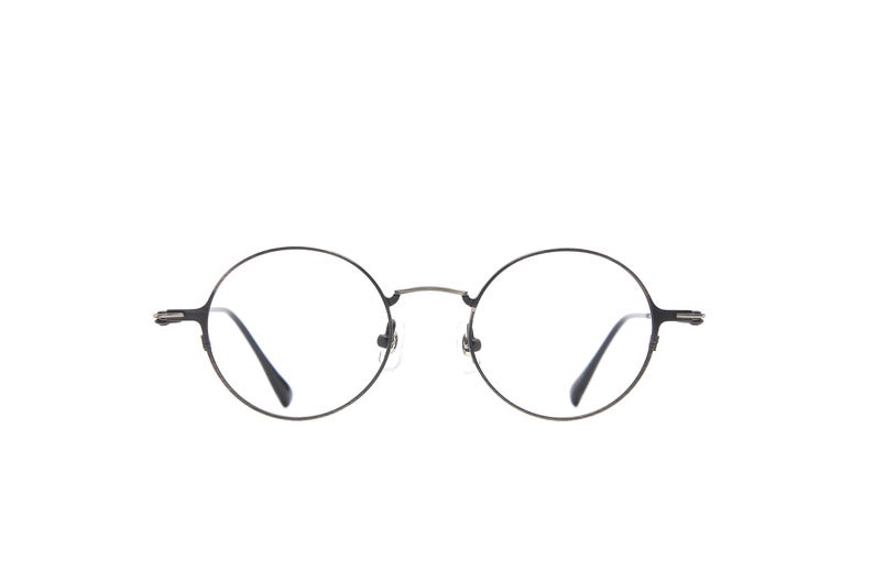 May include: Round eyeglasses featuring a thin, dark metallic frame with a bridge connecting the circular lenses. The temples are slender and extend outward from the sides, ending in curved tips. The design is simple, focusing on the circular shape.