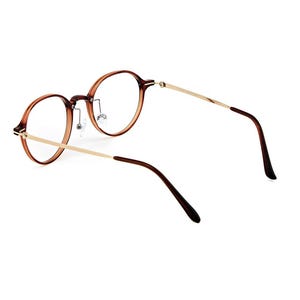 May include: Round eyeglasses featuring translucent brown acetate rims and thin gold-tone metal temples. The frame includes adjustable nose pads and dark brown temple tips, providing a clear view of the circular lenses and the structural bridge.
