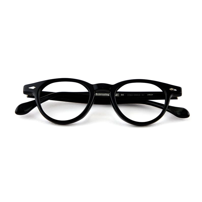 May include: Black, round-framed eyeglasses with a keyhole bridge. The glasses have a classic design with thick rims and temples. The text "Reinventing" is visible on the frame. The eyeglasses are set against a white background.