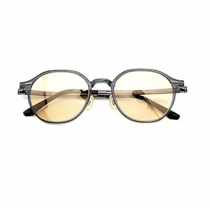 May include: Round-framed glasses featuring a translucent dark gray acetate frame and light amber-tinted lenses. The eyewear includes integrated nose pads and thin temples, showcasing a clear, neutral design suitable for everyday optical wear.