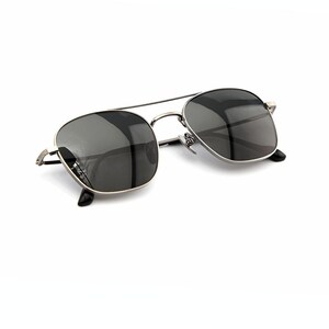 May include: Sunglasses featuring a thin, metallic silver-toned frame with a double bridge design. The lenses are dark gray and semi-transparent, with black temple tips visible at the ends of the thin metal arms, providing a sleek and functional look.