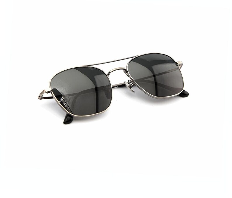 May include: Sunglasses featuring a thin, metallic silver-toned frame with a double bridge design. The lenses are dark gray and semi-transparent, with black temple tips visible at the ends of the thin metal arms, providing a sleek and functional look.