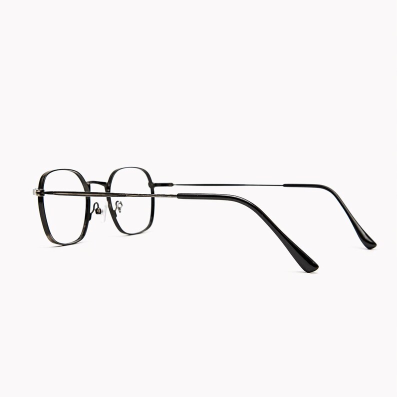 May include: A pair of eyeglasses with thin, dark-toned metal frames and a rounded square shape. The glasses feature adjustable nose pads, slender temples, and curved black plastic tips at the ends of the arms for a secure fit behind the ears.
