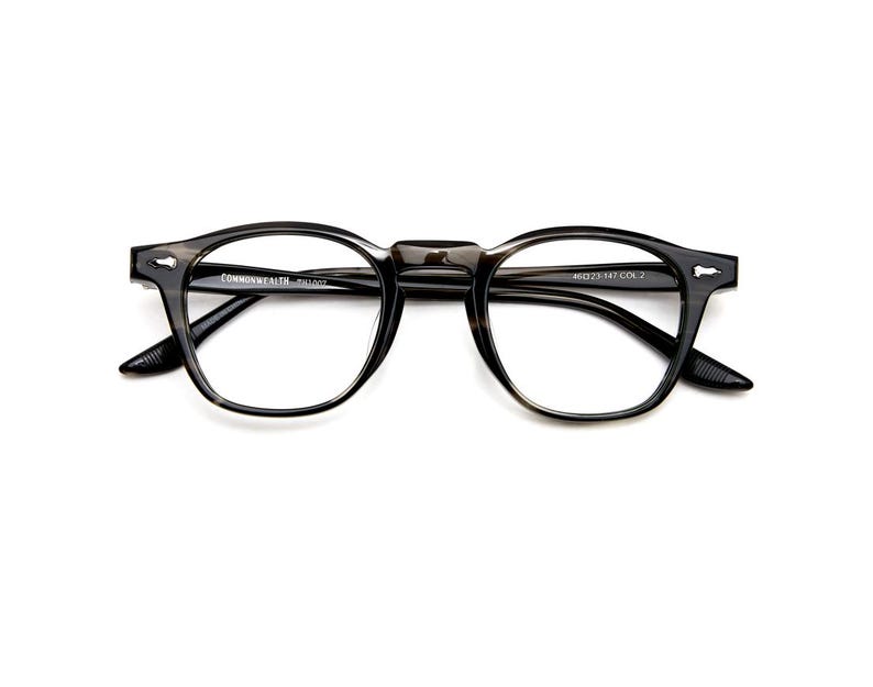 May include: A pair of eyeglasses with a dark, speckled frame. The glasses have a classic, round shape with a keyhole bridge. The text "COMMONWEALTH - R1007" is printed on the frame. The lenses are clear.
