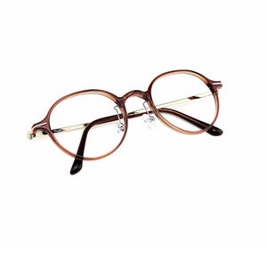 May include: Round eyeglasses featuring a translucent brown acetate frame with thin gold-tone metal temples. The inner left temple is inscribed with the word Think. The glasses include clear lenses, a bridge, and adjustable nose pads for support.