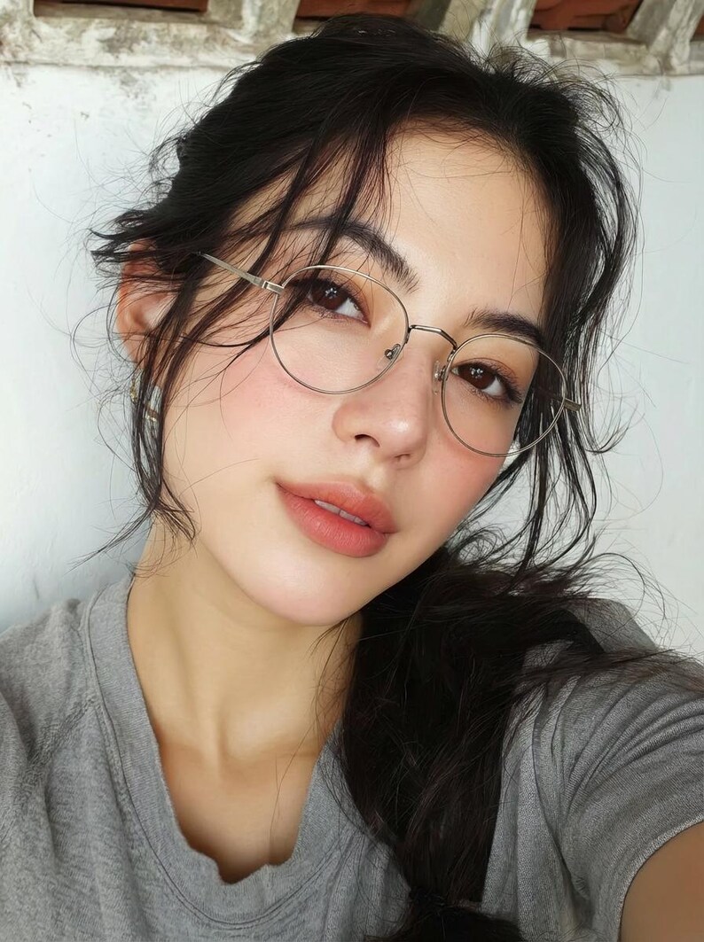 Puede incluir: Un par de gafas de montura met&aacute;lica fina y forma ovalada con acabado plateado. El armaz&oacute;n presenta un puente minimalista y patillas delgadas, sobre un rostro de cabello oscuro que viste una camiseta gris de cuello redondo.