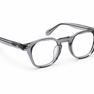 May include: A pair of gray, round-framed eyeglasses. The frames are a translucent gray color, with a classic design. The lenses are clear, and the temples extend to the sides. The glasses are set against a white background.