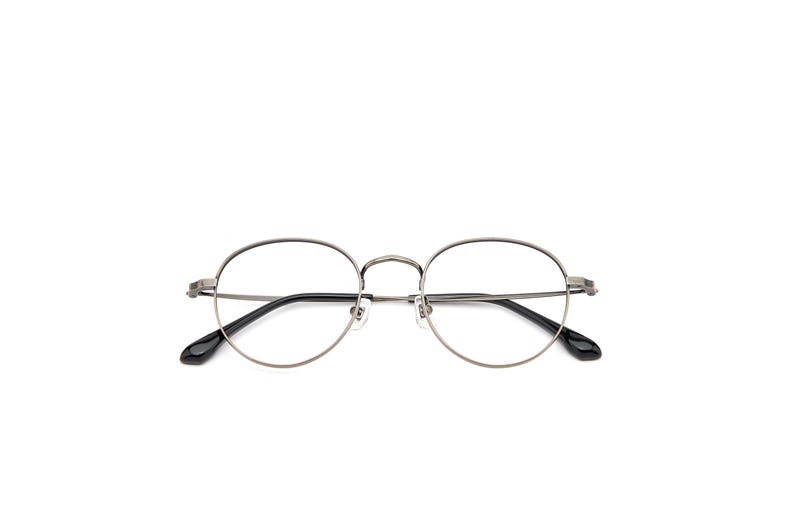 Puede incluir: Gafas redondas con una montura met&aacute;lica fina de color gris plomo. El dise&ntilde;o incluye un puente estrecho, almohadillas nasales ajustables y varillas delgadas que terminan en puntas de acetato negro, permitiendo una visi&oacute;n clara de los cristales.